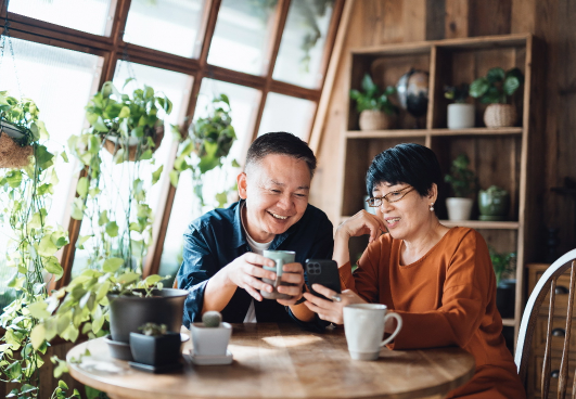 image of asian couple sitting at a table in a home setting to a bank of windows with lots of plants