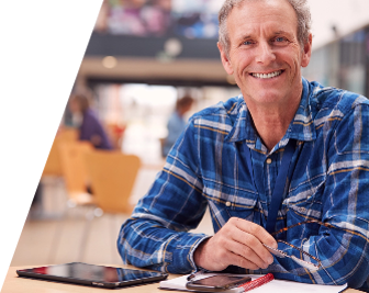 Image of man in blue checked shirt resting elbows on a table with ipad, iphone and notebook