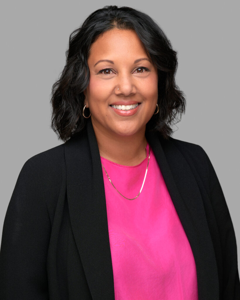 A woman wearing a pink shirt and black blazer smiling